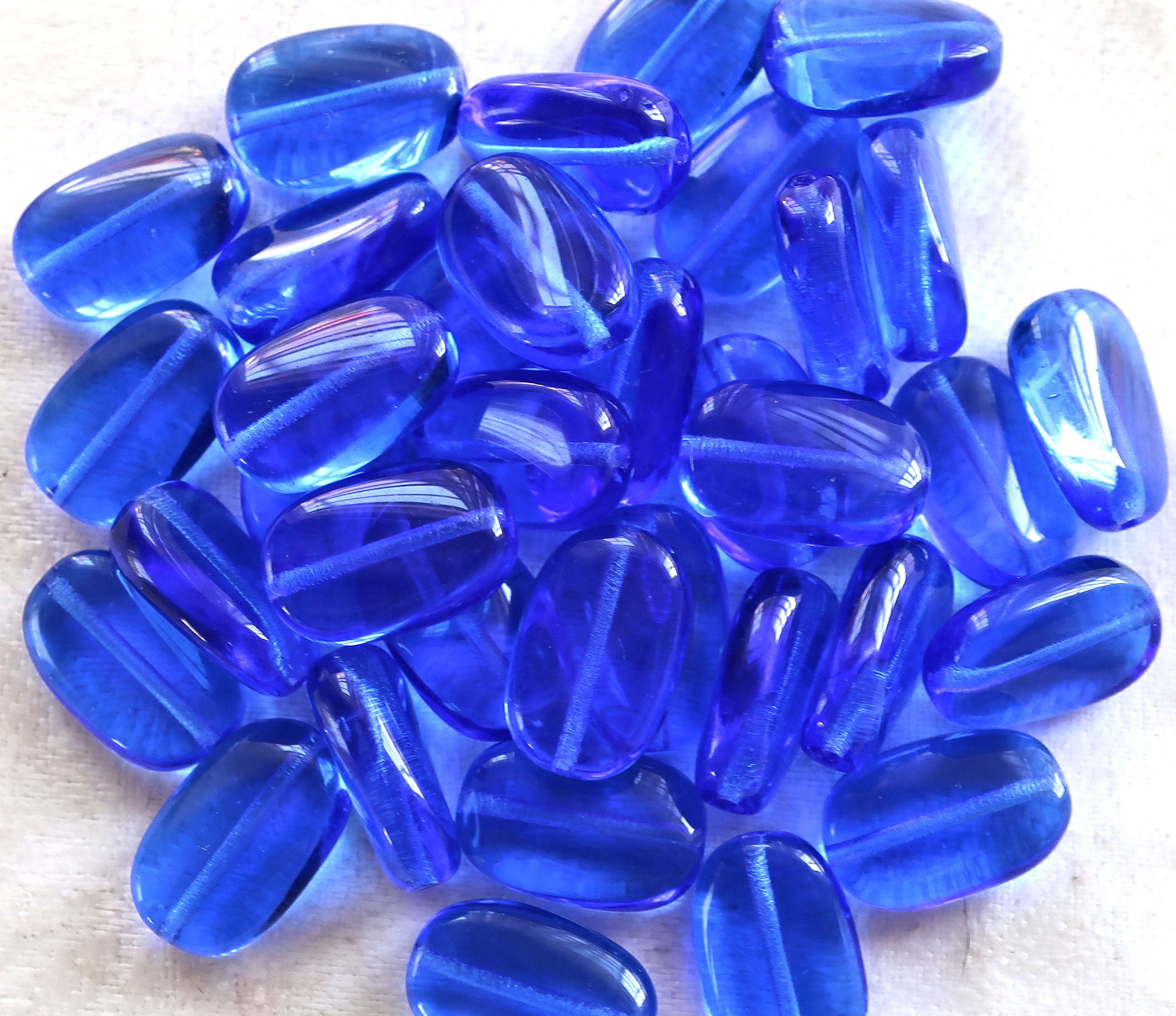 Lot of 25 transparent Sapphire Blue slightly twisted oval Czech Glass beads, 14mm x 8mm pressed glass beads C7325 - Glorious Glass Beads