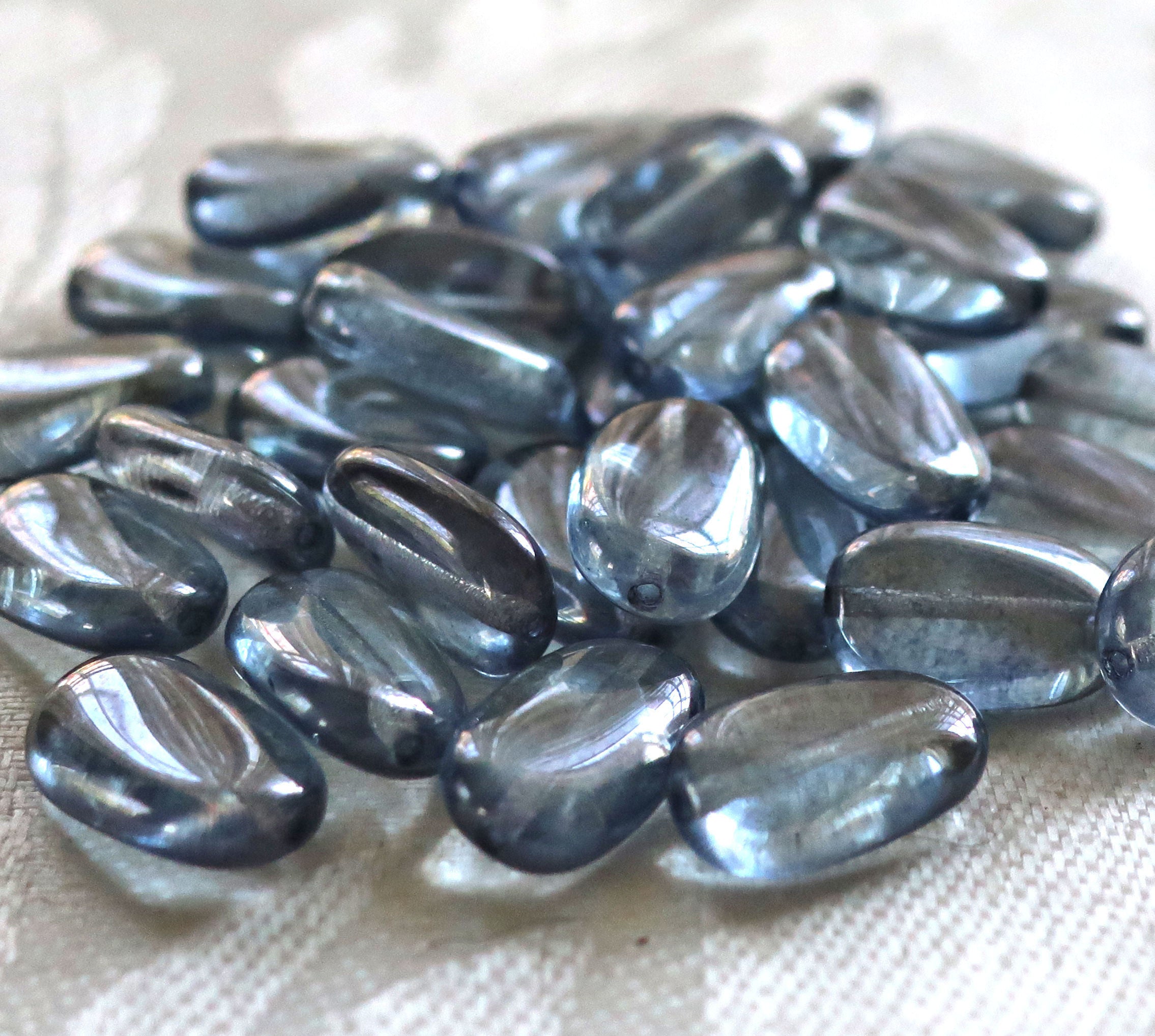 Lot of 25 transparent Lumi Blue slightly twisted oval Czech Glass beads, 14mm x 8mm pressed glass beads C5625 - Glorious Glass Beads